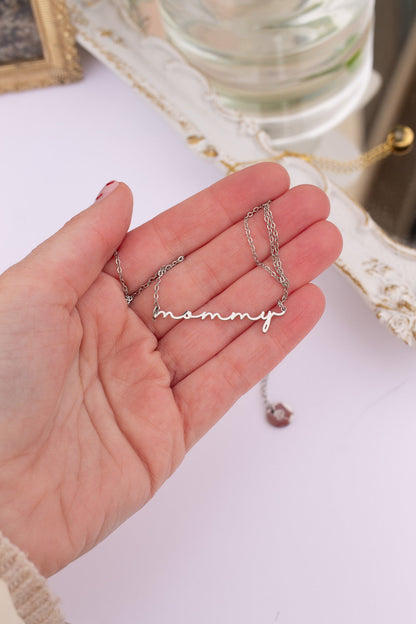 Hand holding a silver 'mommy' necklace on a light background