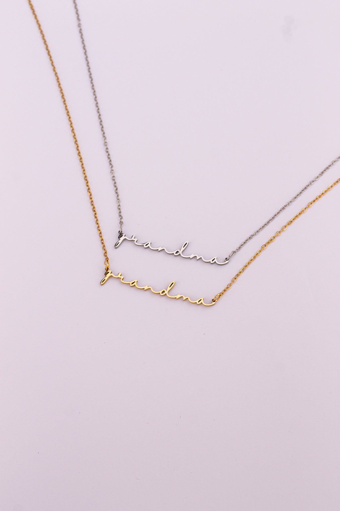 Two gold necklaces with 'grandma' engraved on a light pink background