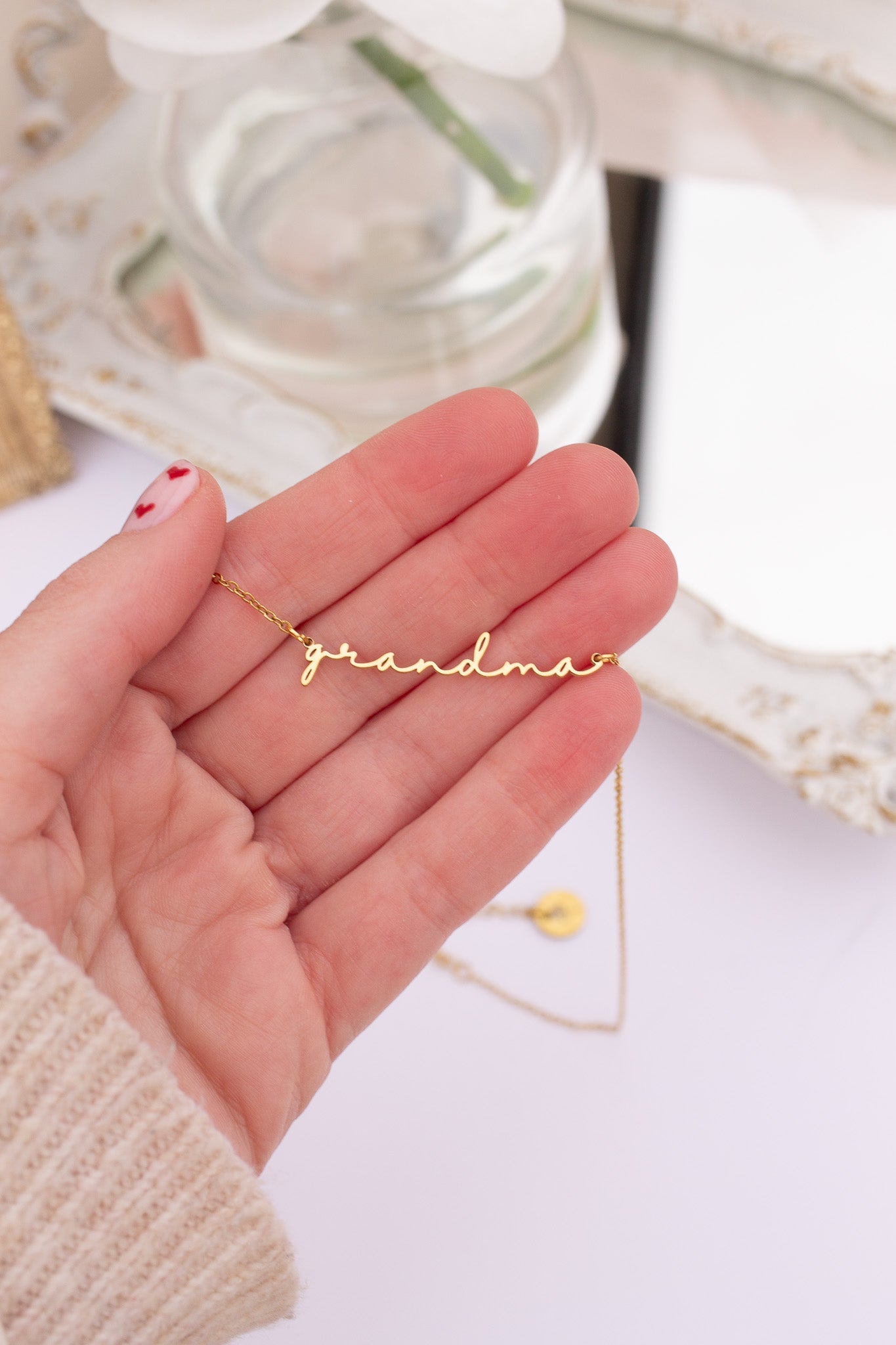 Gold necklace with 'grandma' pendant held in a hand against a light background
