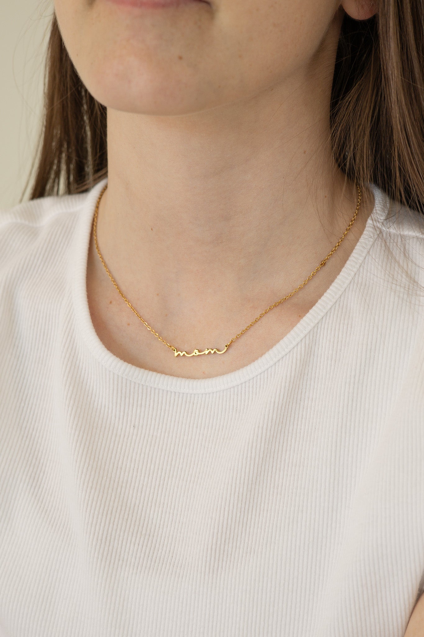 Gold necklace worn by a person against a neutral background