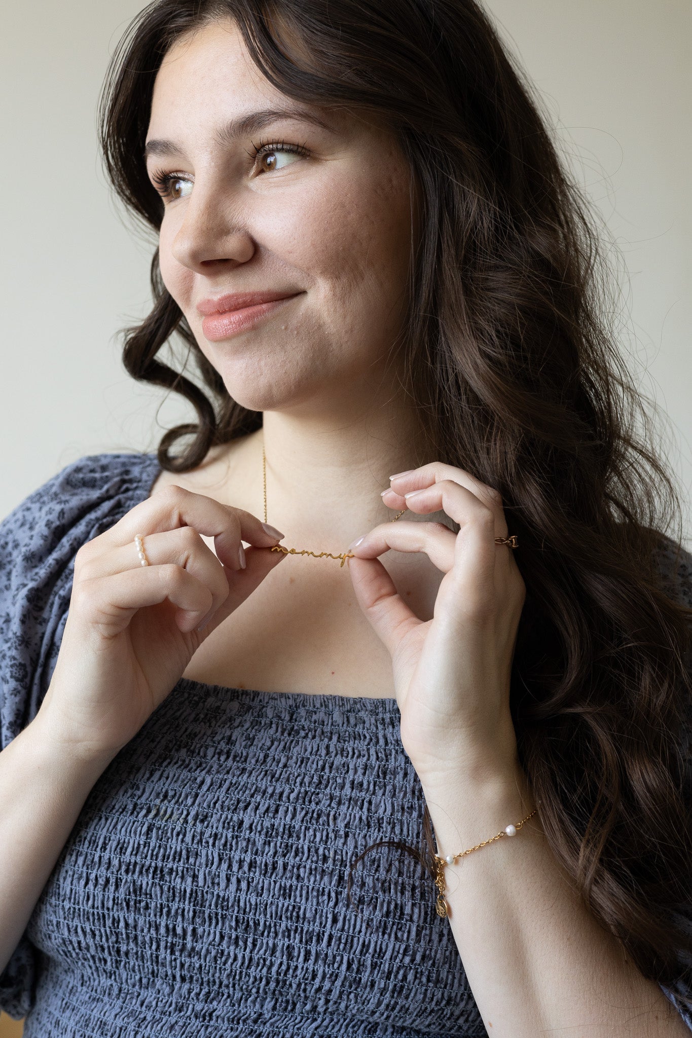 Woman wearing a necklace, smiling against a neutral background
