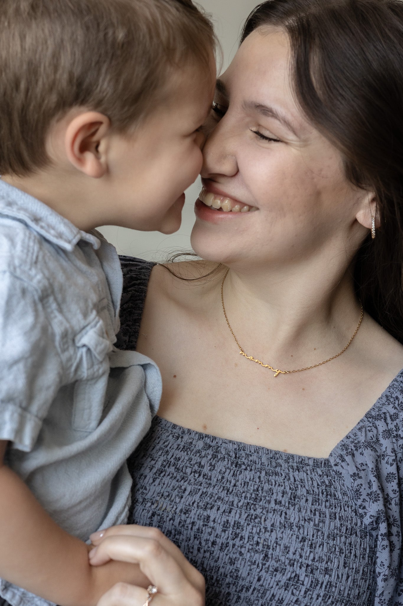 Woman and child smiling at each other with a close-up view of the woman's "mommy" necklace.