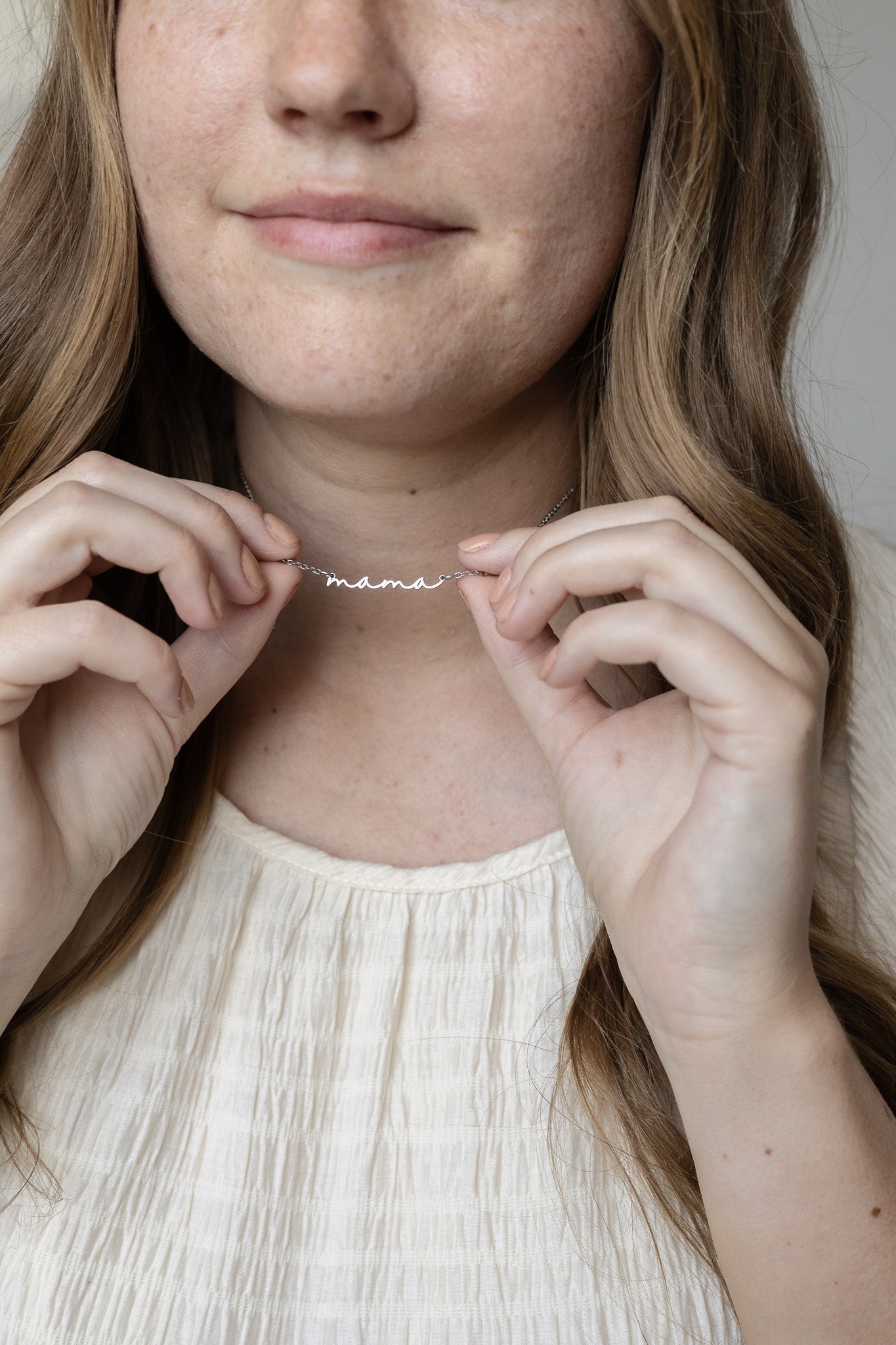 Person wearing a 'mama' necklace with a neutral background