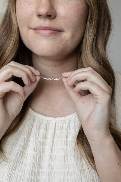 Person wearing a 'mama' necklace with a neutral background