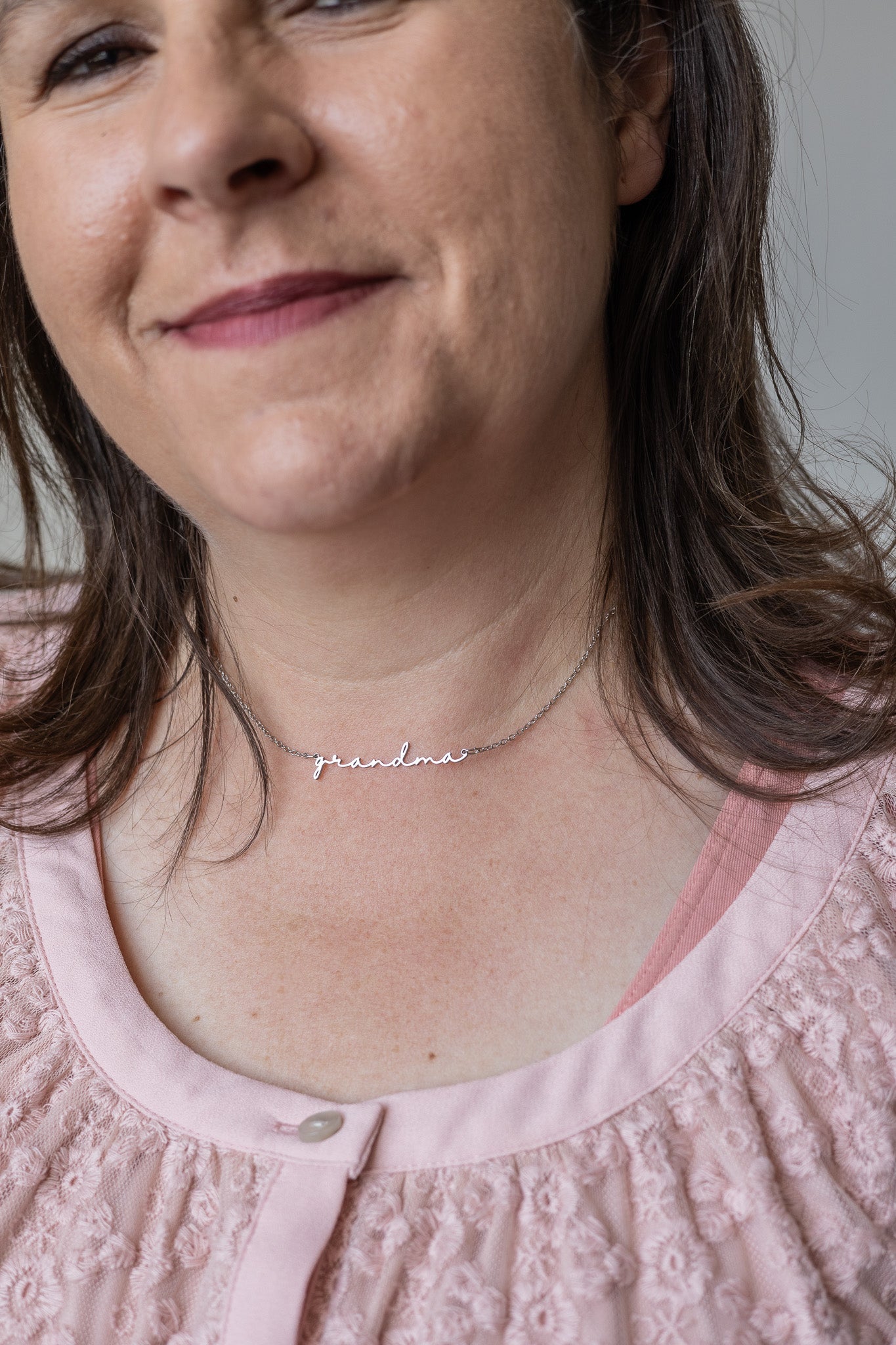 Woman wearing a necklace with the word 'grandma' on a plain background