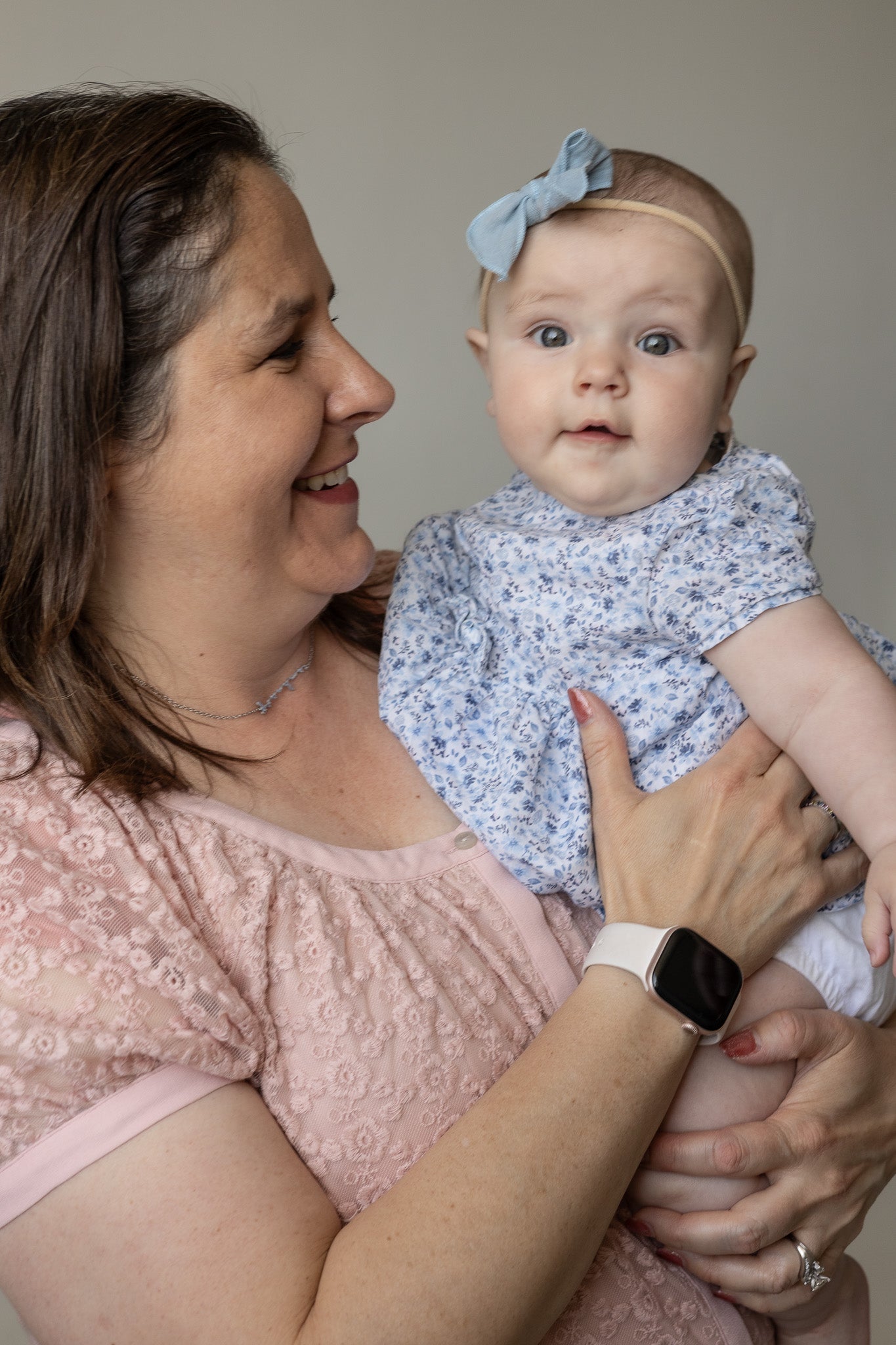 Woman holding a baby wearing a floral outfit and headband against a plain background