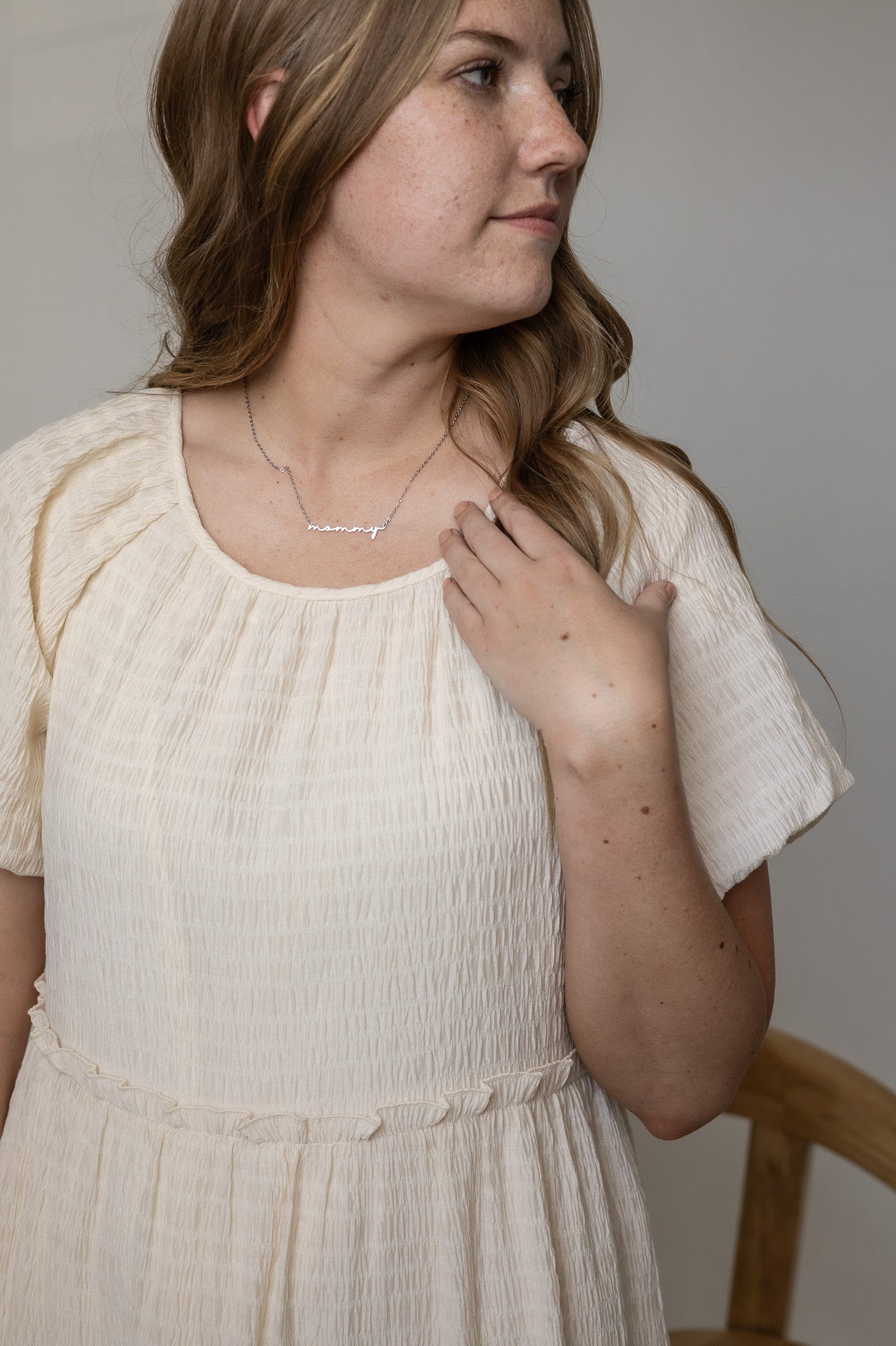 Woman wearing a white dress and necklace against a neutral background