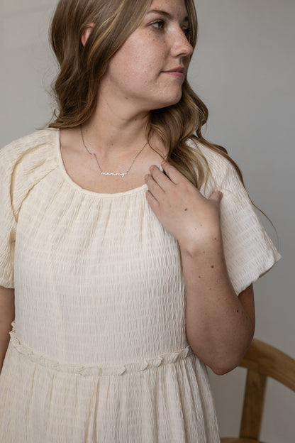 Woman wearing a white dress and necklace against a neutral background