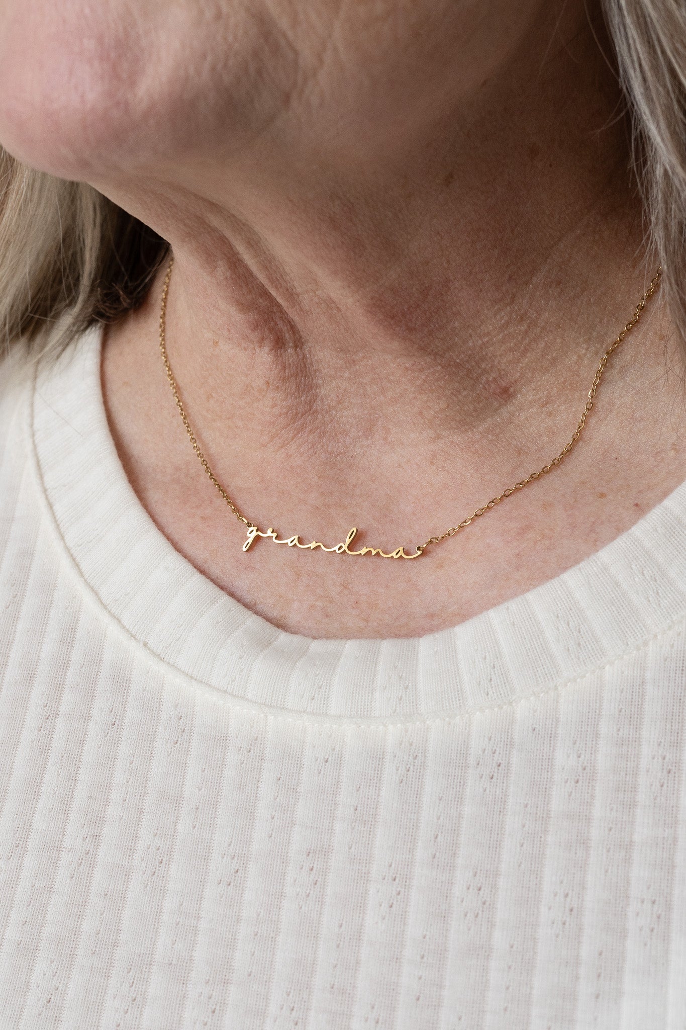 Gold necklace with engraved name on a person wearing a white shirt