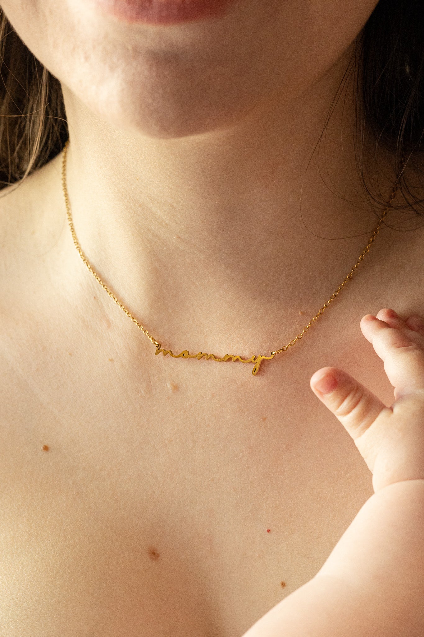 Gold "mommy" necklace worn by a person with a baby's hand near the chest.