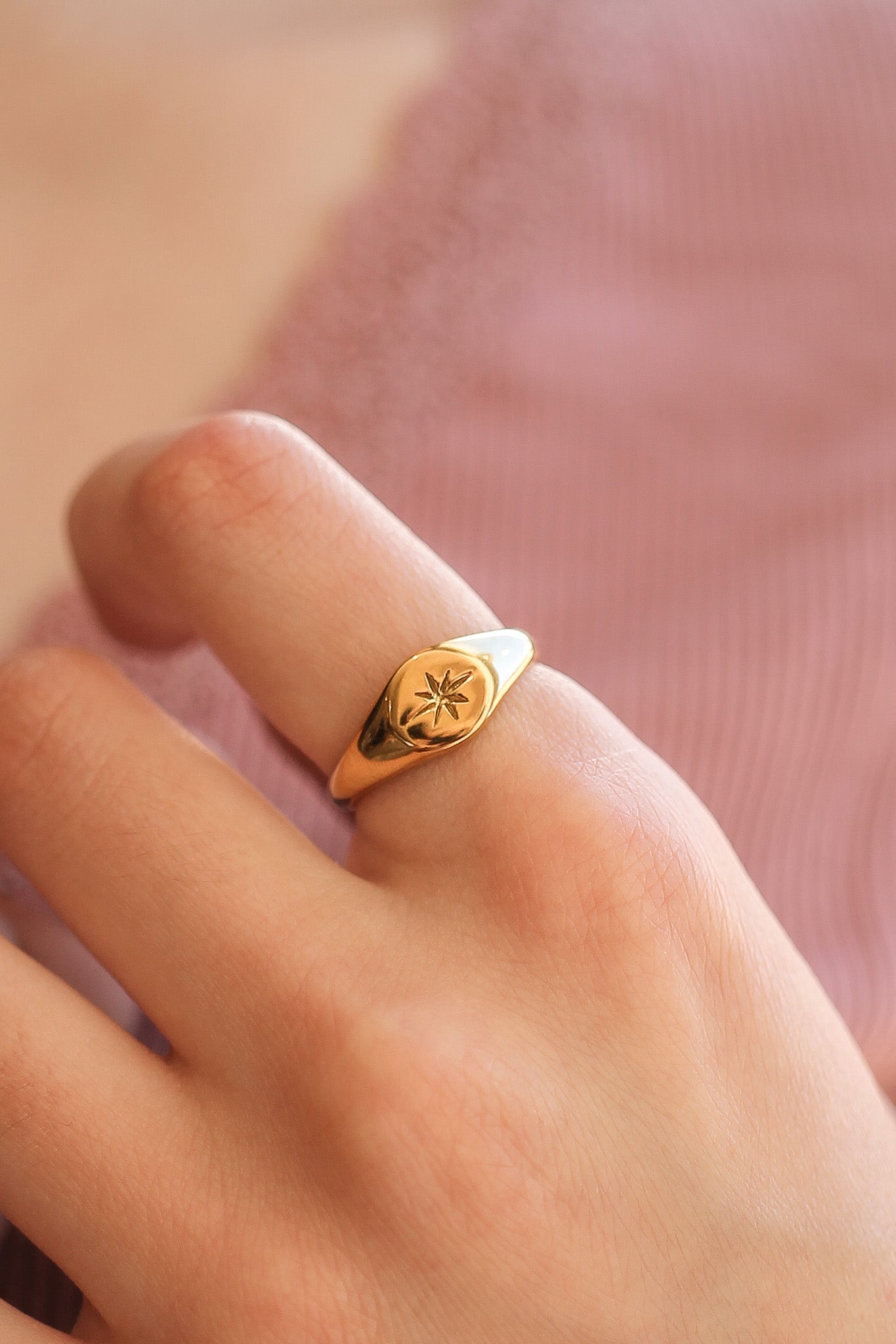 Gold ring with a floral design on a person's finger against a pink fabric background