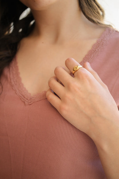 Close-up of a person wearing a gold ring on a pink garment.