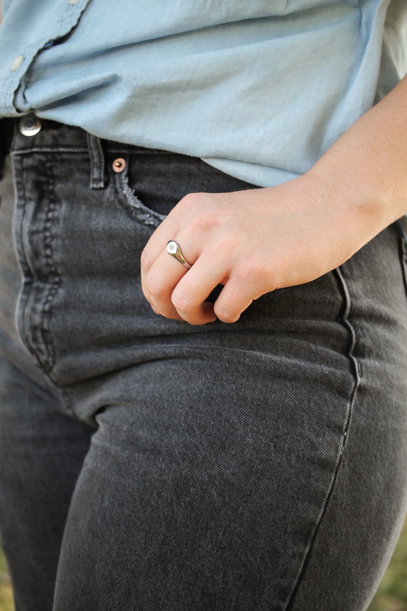 Person wearing gray jeans and a light blue shirt with a ring on their finger.