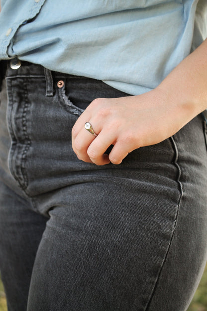 Person wearing gray jeans and a light blue shirt with a ring on their finger.
