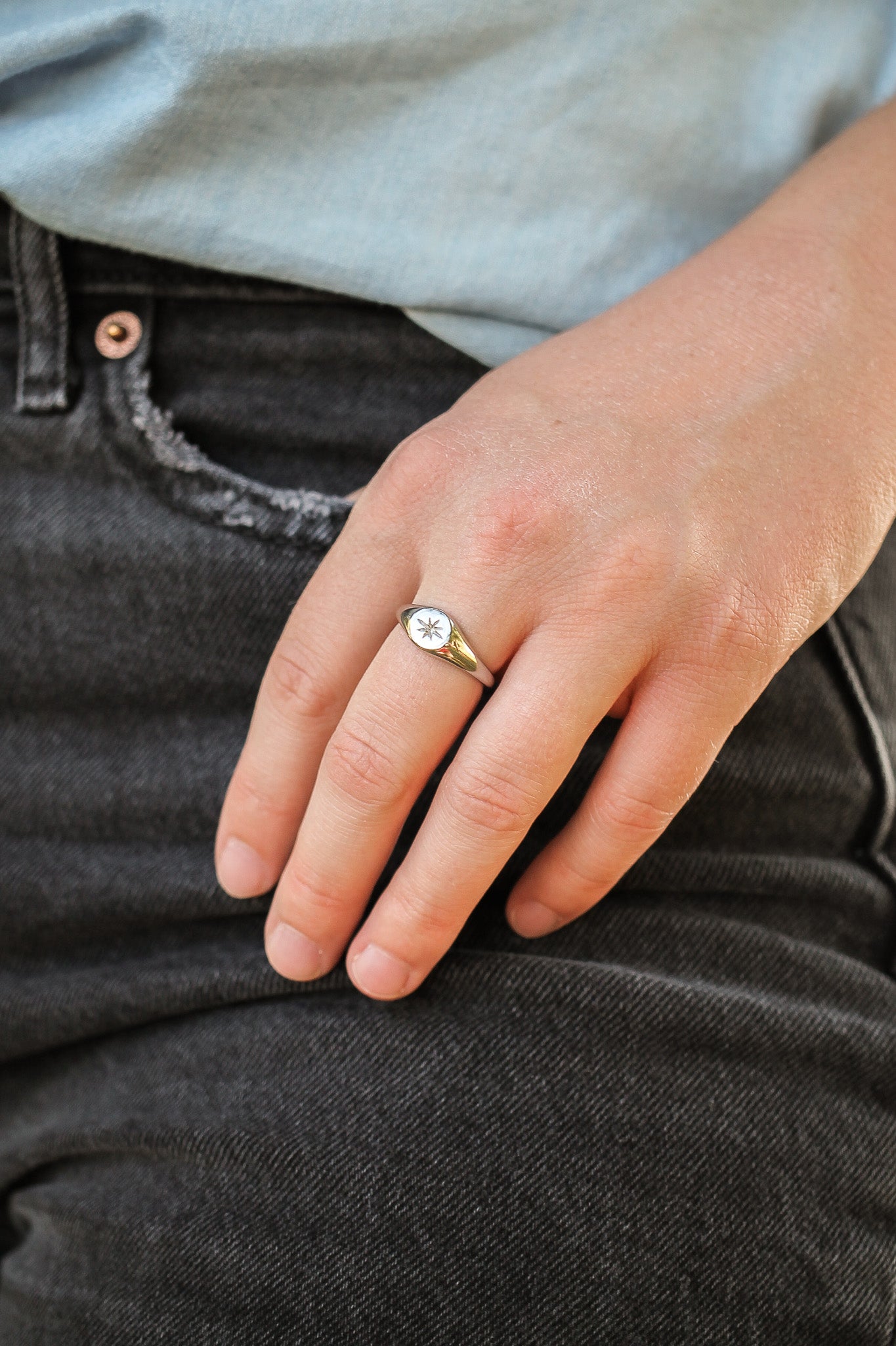 Close-up of a hand wearing a gold ring with a diamond, resting on dark jeans.