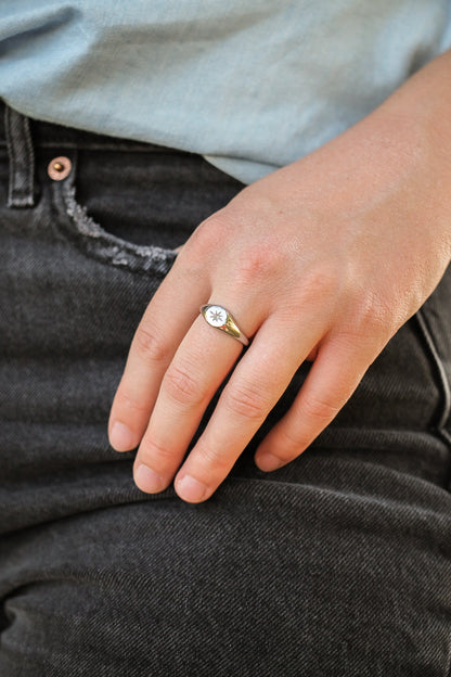 Close-up of a hand wearing a gold ring with a diamond, resting on dark jeans.