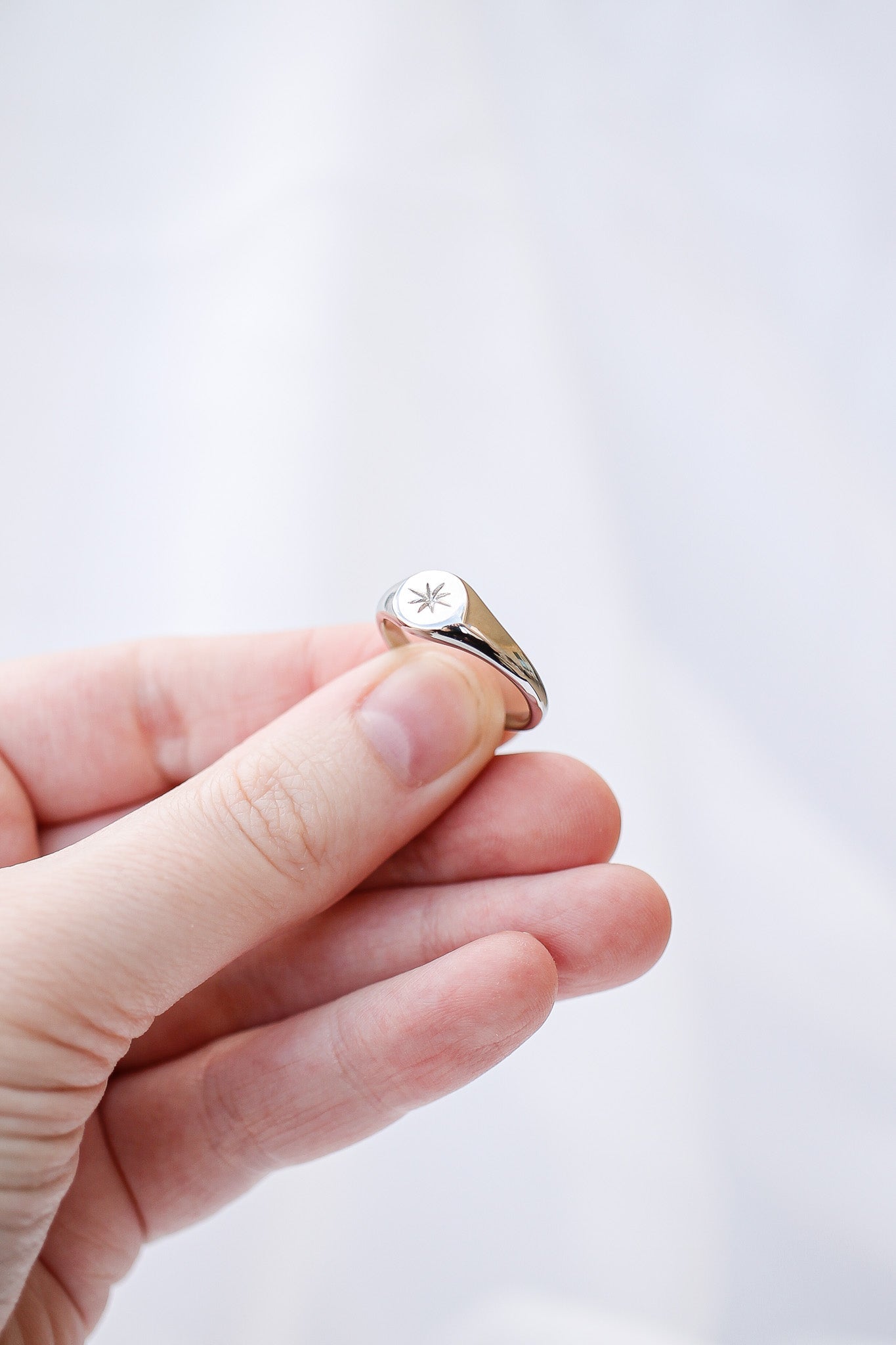 Hand holding a silver ring with a clear gemstone against a light gray background