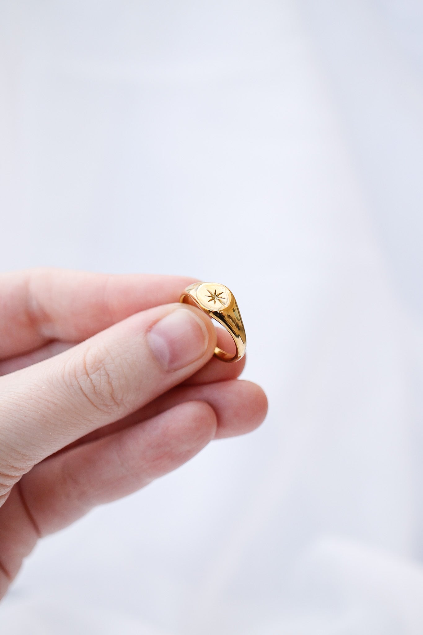 Gold ring with a star design held between fingers against a light background
