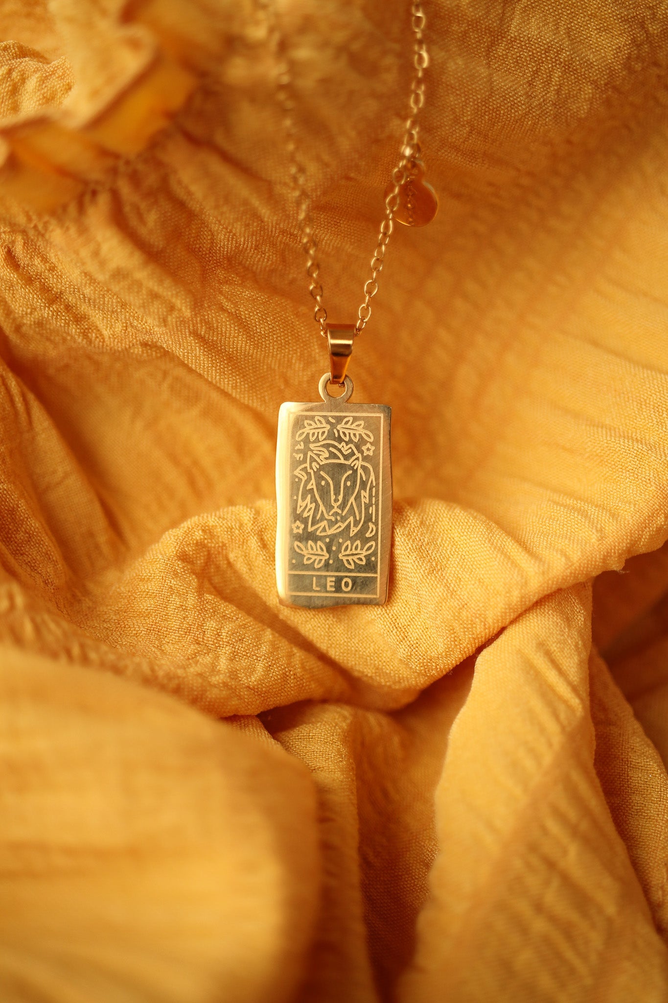 Gold necklace with a Leo pendant on a yellow fabric background