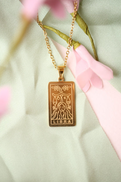 Gold Libra zodiac pendant necklace on a light green fabric background