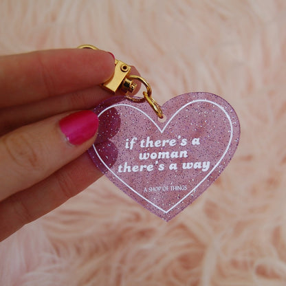 Heart-shaped keychain with motivational quote held by a hand against a soft pink background