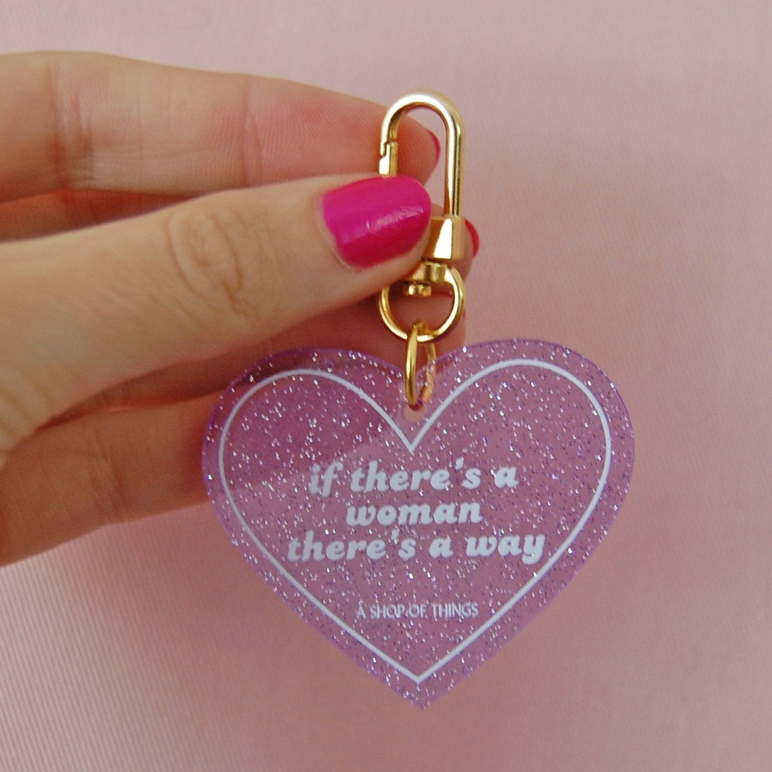 Heart-shaped keychain with motivational quote held by a hand on a pink background