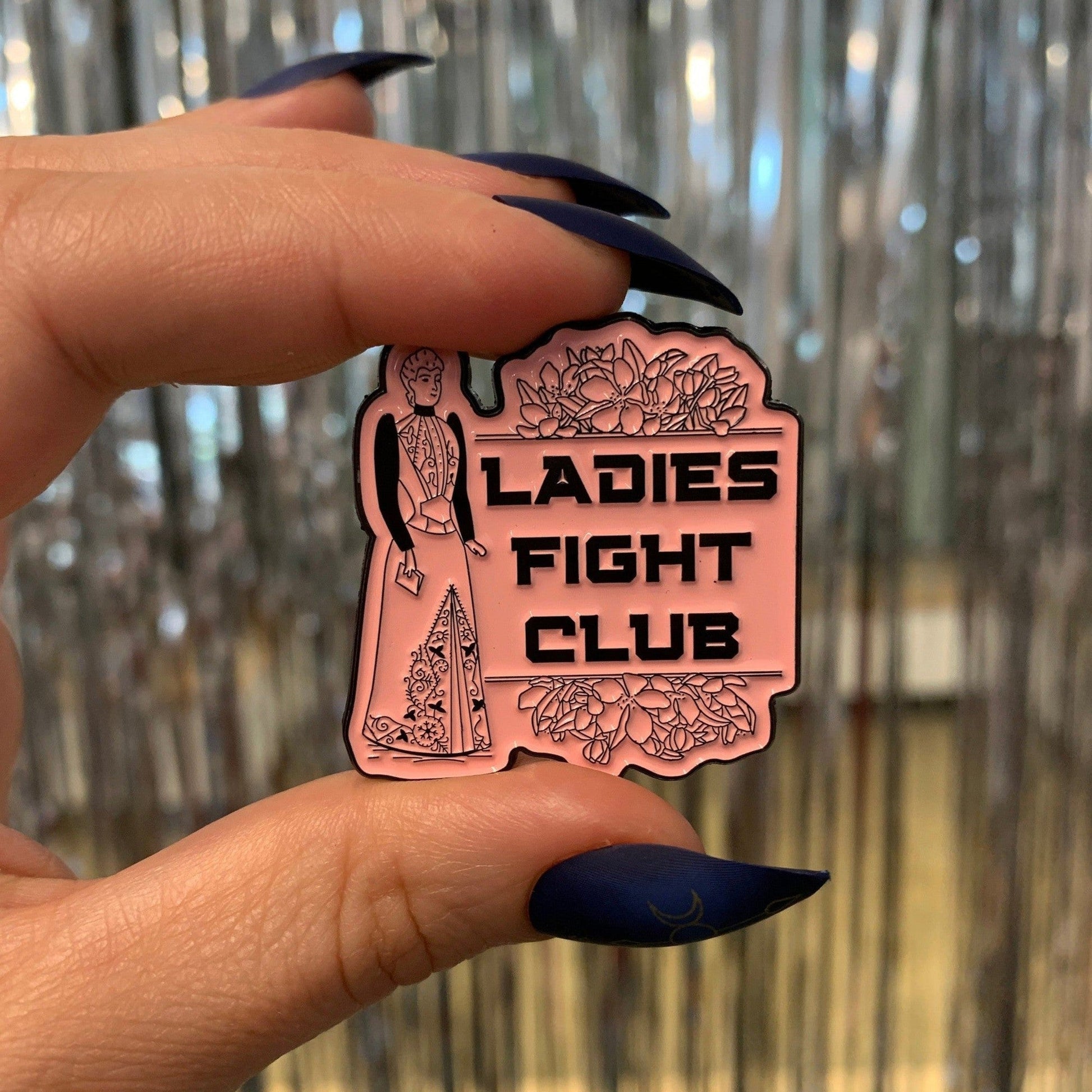 Pin with 'Ladies Fight Club' text held by a hand against a metallic background