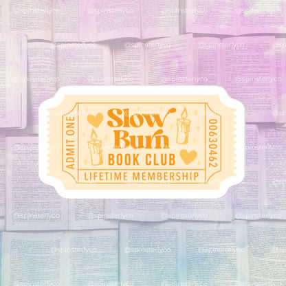 A stylized ticket-shaped graphic reading 'Slow Burn Book Club Lifetime Membership' with candle illustrations, centered over a soft pastel collage of open books. The design appears to be the product artwork itself rather than a real-world scene, so Product/Packaging fits better than Lifestyle or Scenery.