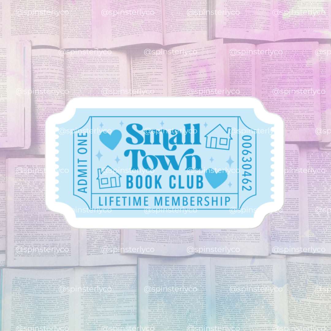 A die-cut sticker designed like a vintage boarding pass with the text 'Small Town Book Club' and 'LIFETIME MEMBERSHIP' in light blue on a white background, shown against a soft-focus background of open books.