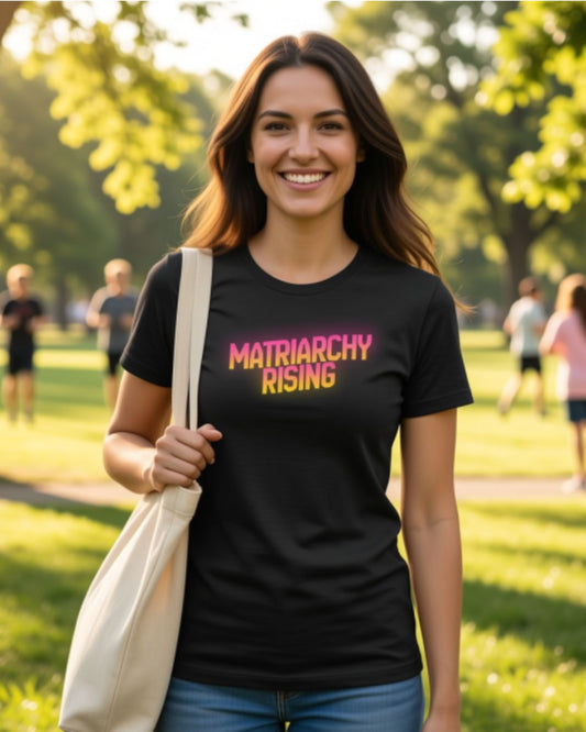 Woman wearing a black t-shirt with 'Matriarchy Rising' text in a park.