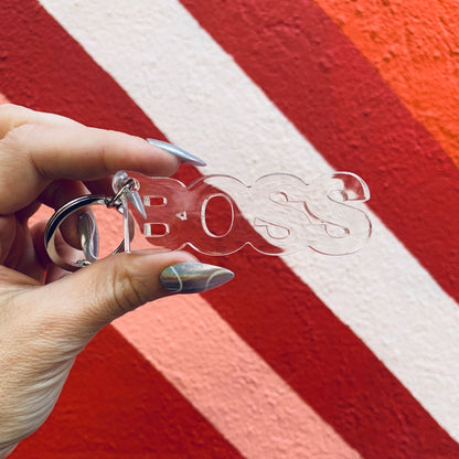 Hand holding a clear 'BOSS' keychain against a red and white striped background