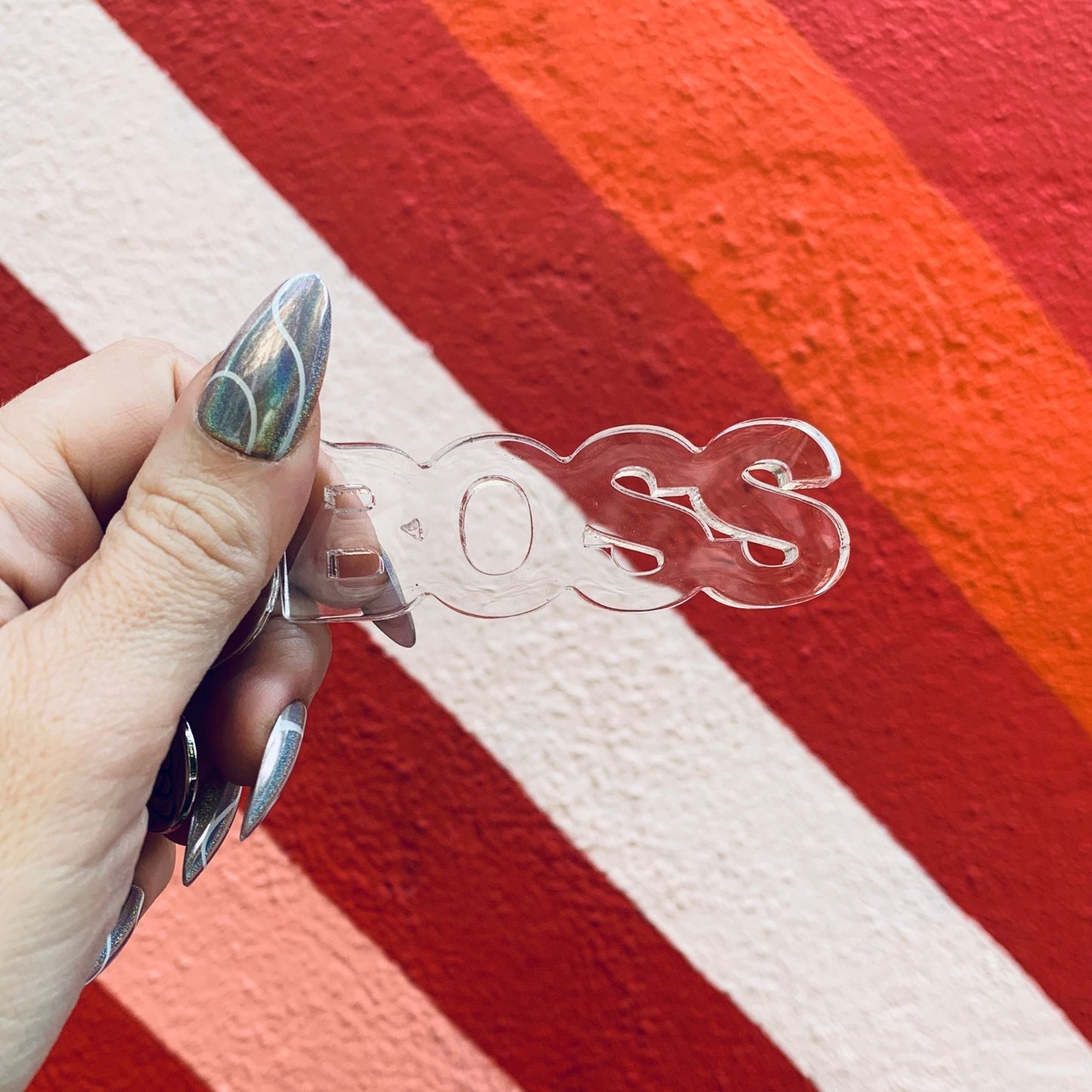 Hand holding a clear plastic item with 'BOSS' branding against a red and white striped background