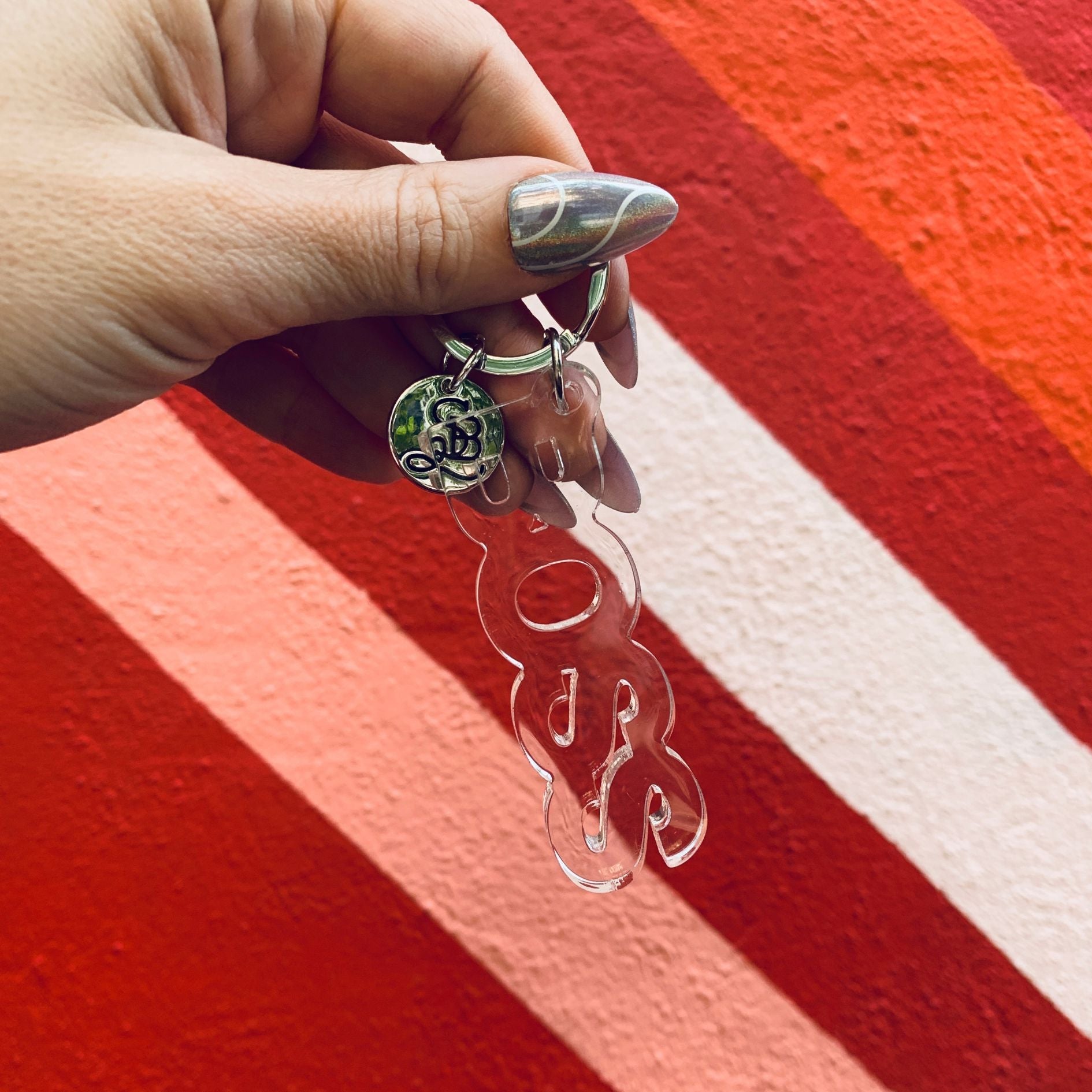 Hand holding a clear keychain with decorative design against a red and white striped background