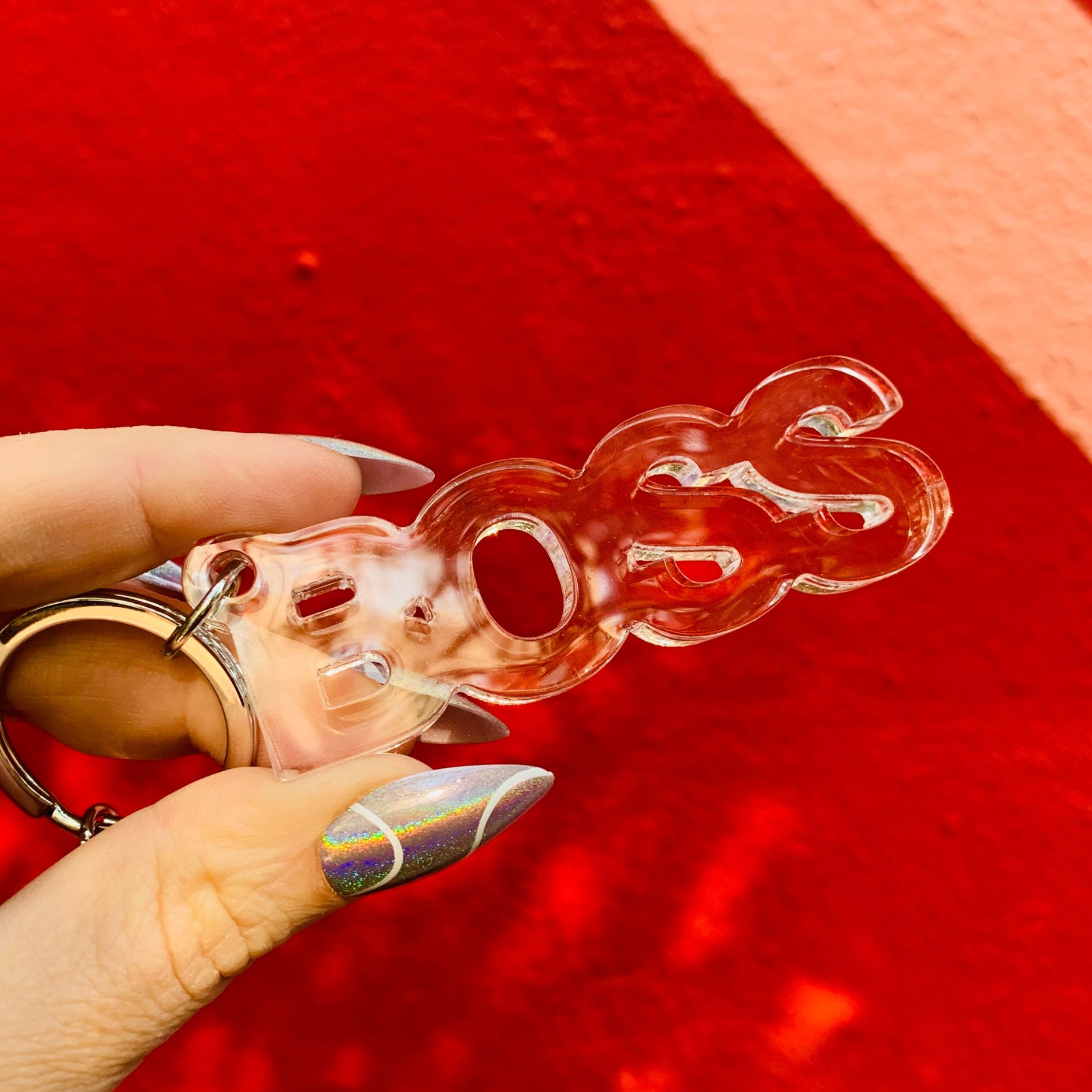 Clear plastic keychain with a unique design held by a hand against a red background