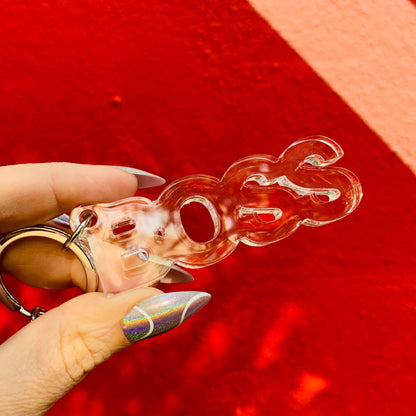 Clear plastic keychain with a unique design held by a hand against a red background