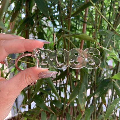 Clear 'BOSS' keychain held by a hand with greenery in the background