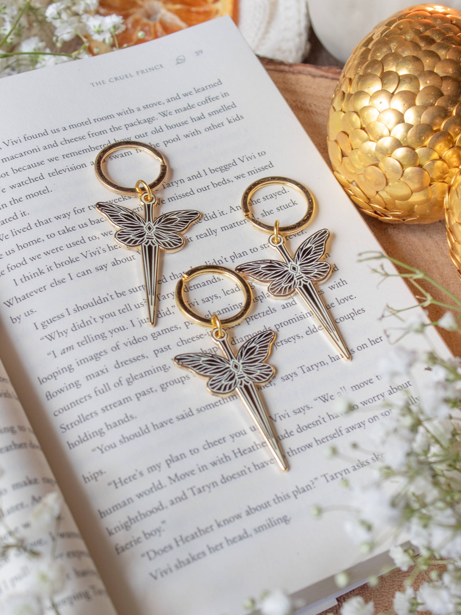 Faerie Dagger Enamel Keychain by Meaggie Moos, gold and purple hard enamel dagger keychain on book page
