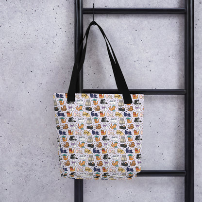 A tote bag with a white background and a colorful pattern of illustrated cats, hanging from a black metal ladder against a textured gray concrete wall.