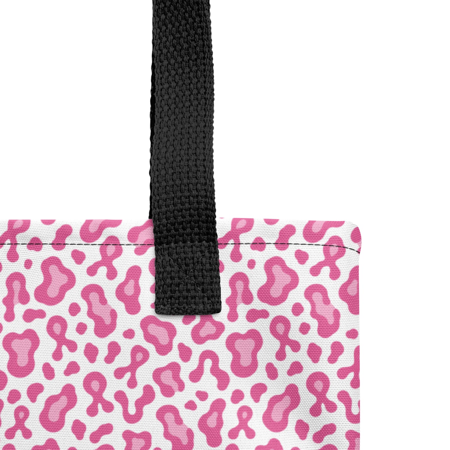 A close-up of a tote bag corner showing a pink and white leopard print pattern with a black woven handle on a white background.