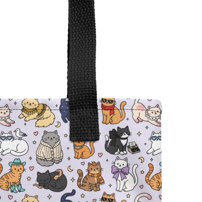 A close-up of a tote bag corner showing a white fabric body printed with a colorful cartoon cat pattern and a black woven handle, photographed against a white background.