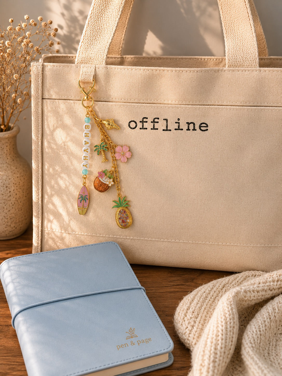 Beige tote bag with 'offline' text, decorative beachy themed bag charm, and blue notebook on a wooden surface.