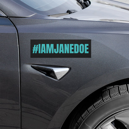 A rectangular black car decal with the text '#IAMJANEDOE' in bright teal, shown applied to the side door of a dark gray vehicle.