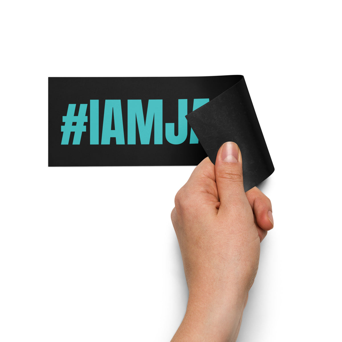 A hand peeling back a black rectangular sticker with the text '#IAMJ' in bright teal, shown against a plain white background.