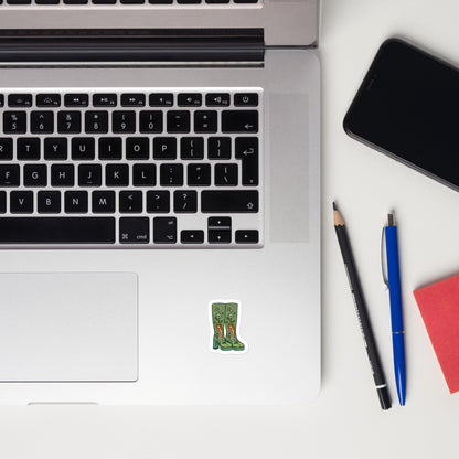 Laptop with a sticker of platform boots with a zodiac inspired design, smartphone, and writing utensils on a white surface