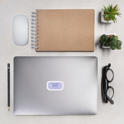 Laptop with a purple book trope lifetime member ticket stub sticker on a desk with a notebook, mouse, pencil, and plants.