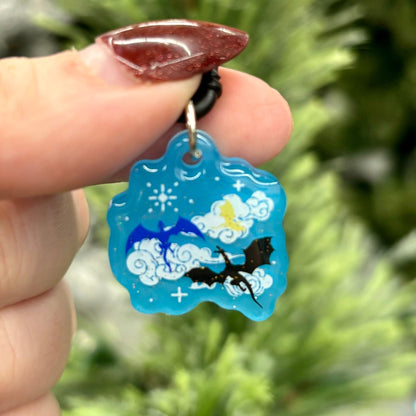 Blue kindle charm with cloud and dragon design held by a hand against a blurred green background