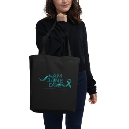 Person holding a black tote bag with 'I AM JANE DOE / ADVOCACY AWARENESS EMPOWERMENT' text in blue.
