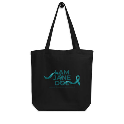 A black canvas tote bag with two shoulder straps, featuring the words 'I AM JANE DOE / ADVOCACY | ACCOUNTABILITY | EMPOWERMENT' in a light blue cursive script with a small airplane graphic above it, shown against a plain white background.