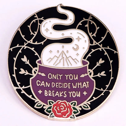 A circular enamel pin featuring a black background with a silver-toned border, a purple cauldron containing white steam with mountains and stars, a red rose at the bottom, and the text 'ONLY YOU CAN DECIDE WHAT BREAKS YOU'.