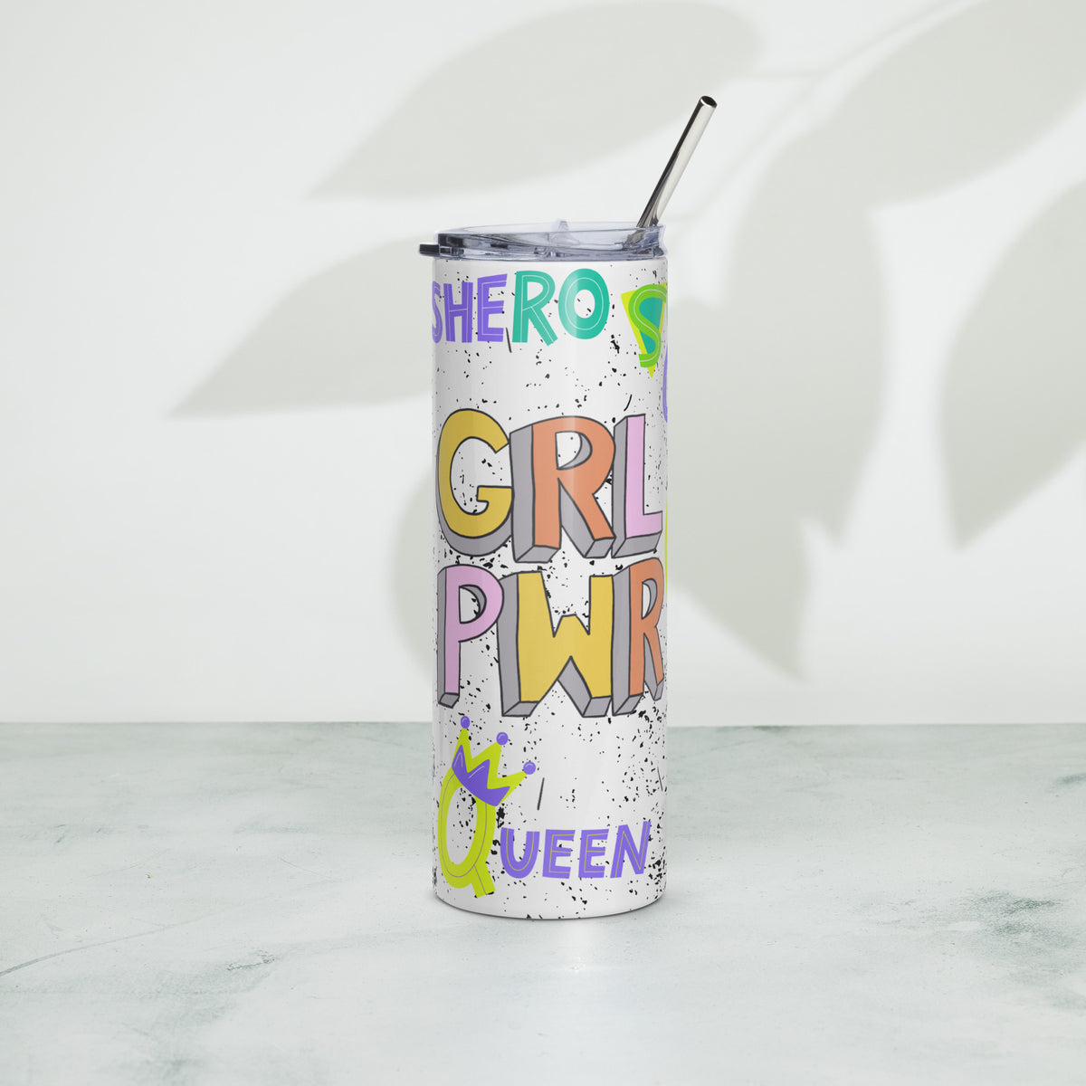A tall, skinny stainless steel tumbler with a clear lid and metal straw, featuring colorful retro-style sticker inspired design with feminist, girl power phrases like 'SHEROES', 'GRL POWER', 'QUEEN' on a white speckled background.